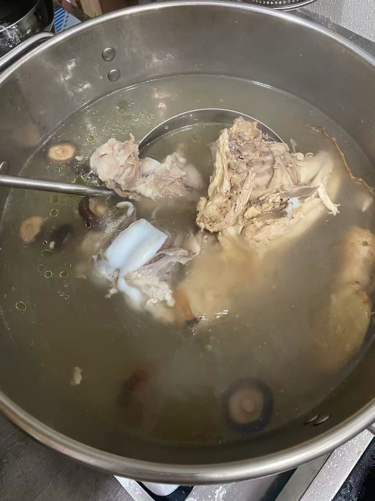 You Yi’s bone stock simmering with chicken and shiitake mushrooms, ladle in hand.